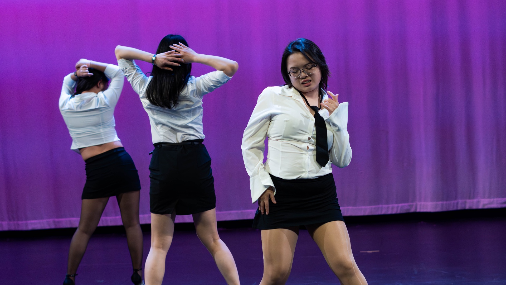 Three dancers performing on a purple-lit stage